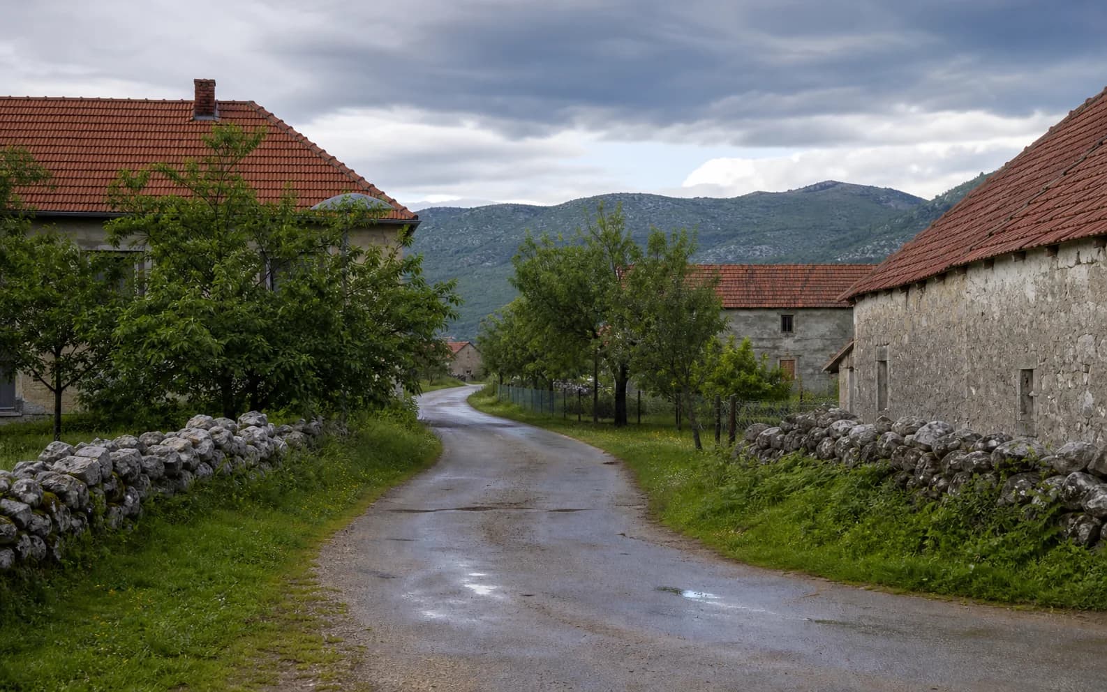 Illustratives Foto für Velika Popina, Gračac: ruhige Siedlungsstraße in hügeliger Umgebung.