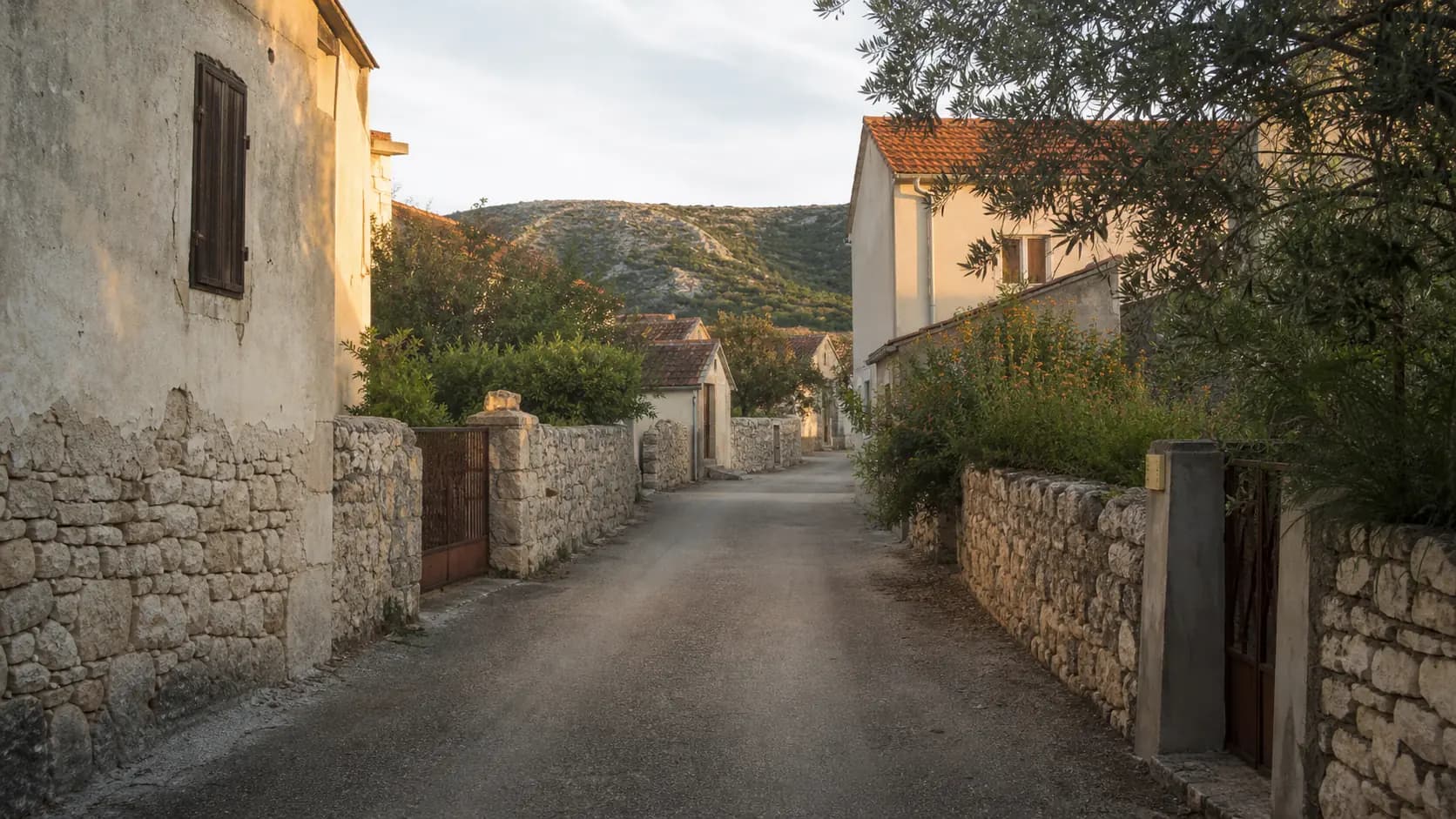 Illustrative quiet village lane with stone walls, homes and a low karst hill in Poljica-Brig.