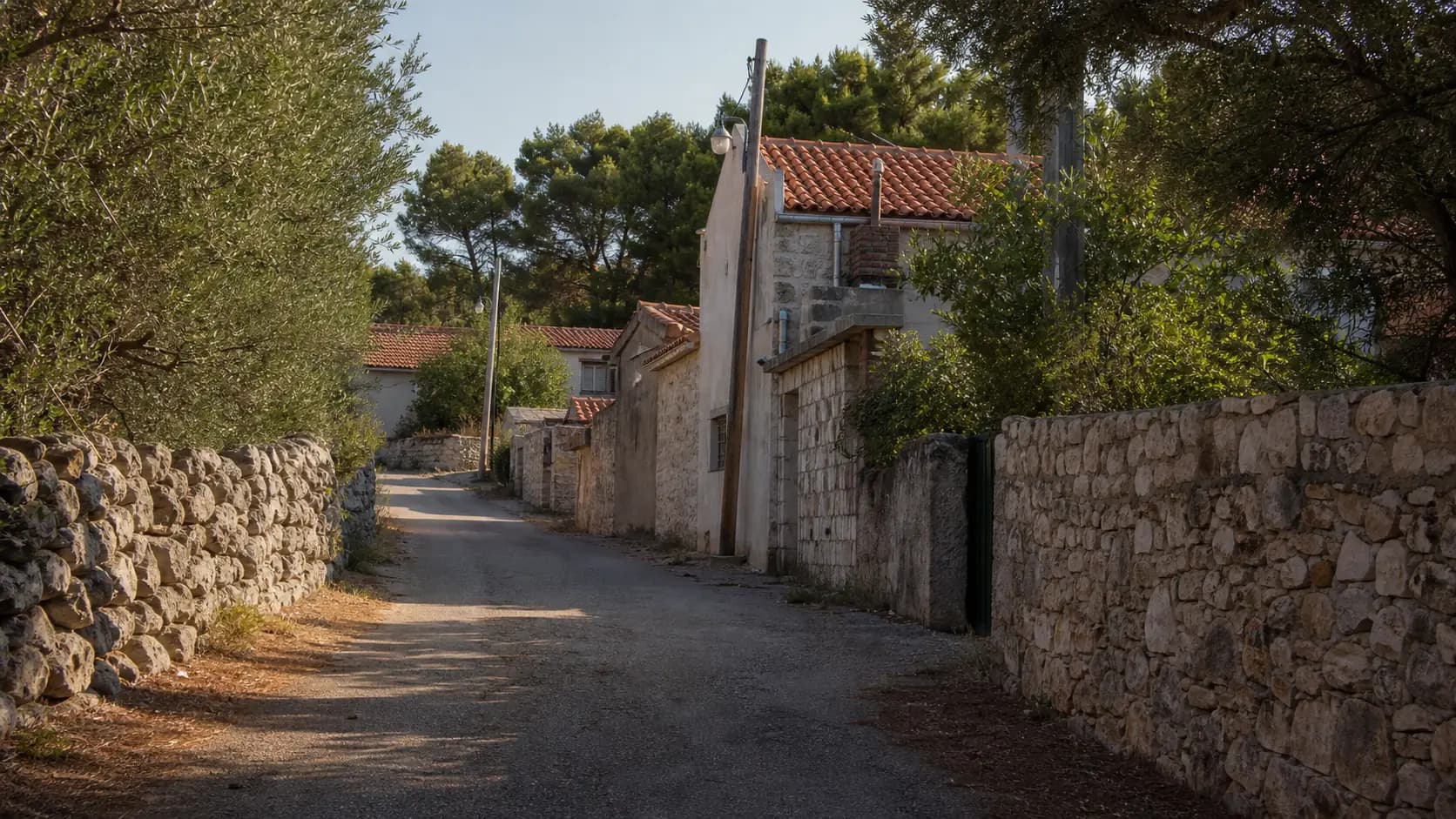 Ilustrativna mirna ulica s kamenim zidovima, mediteranskim kućama i zelenilom u Dragama.