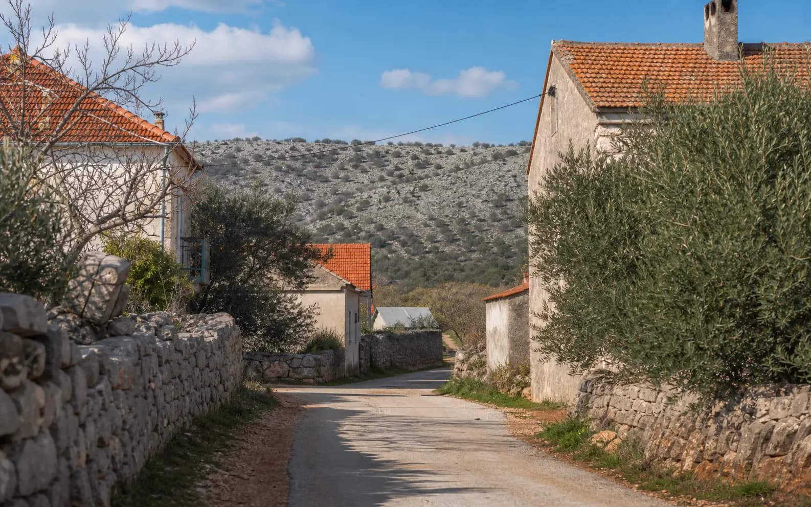 Illustrative ruhige Dorfstraße mit Steinmauern, Häusern und mediterranem Grün im Ambiente von Rupalj.