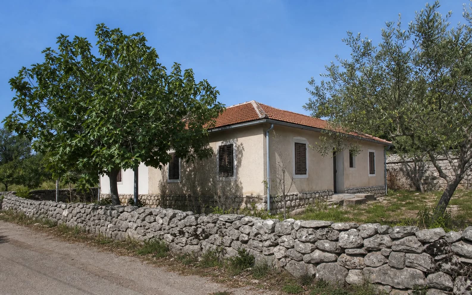 Ilustrativna fotografija za Crljenik, Stankovci: stambeni eksterijer s kamenom, zemljom i zelenilom.