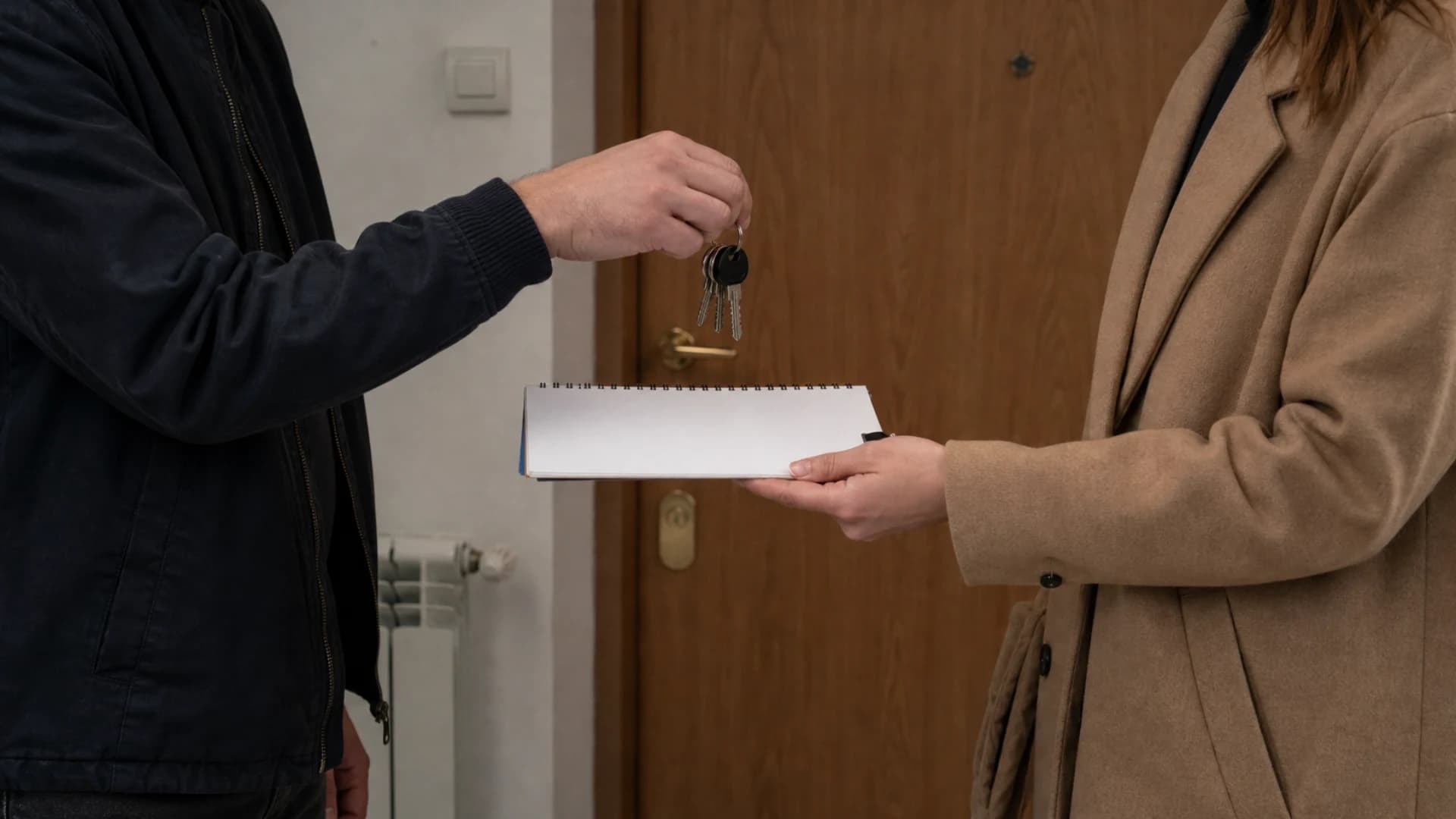 Dvije osobe bez vidljivih lica predaju ključeve uz praznu bilježnicu.