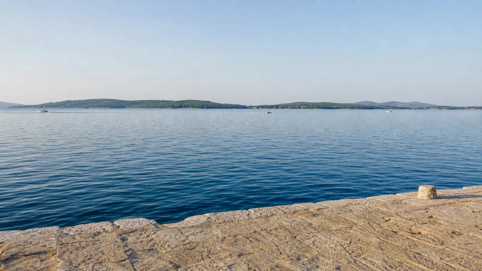 Pogled iz Zadra preko Zadarskog kanala prema zelenom profilu otoka Ugljana u jutarnjem svjetlu.
