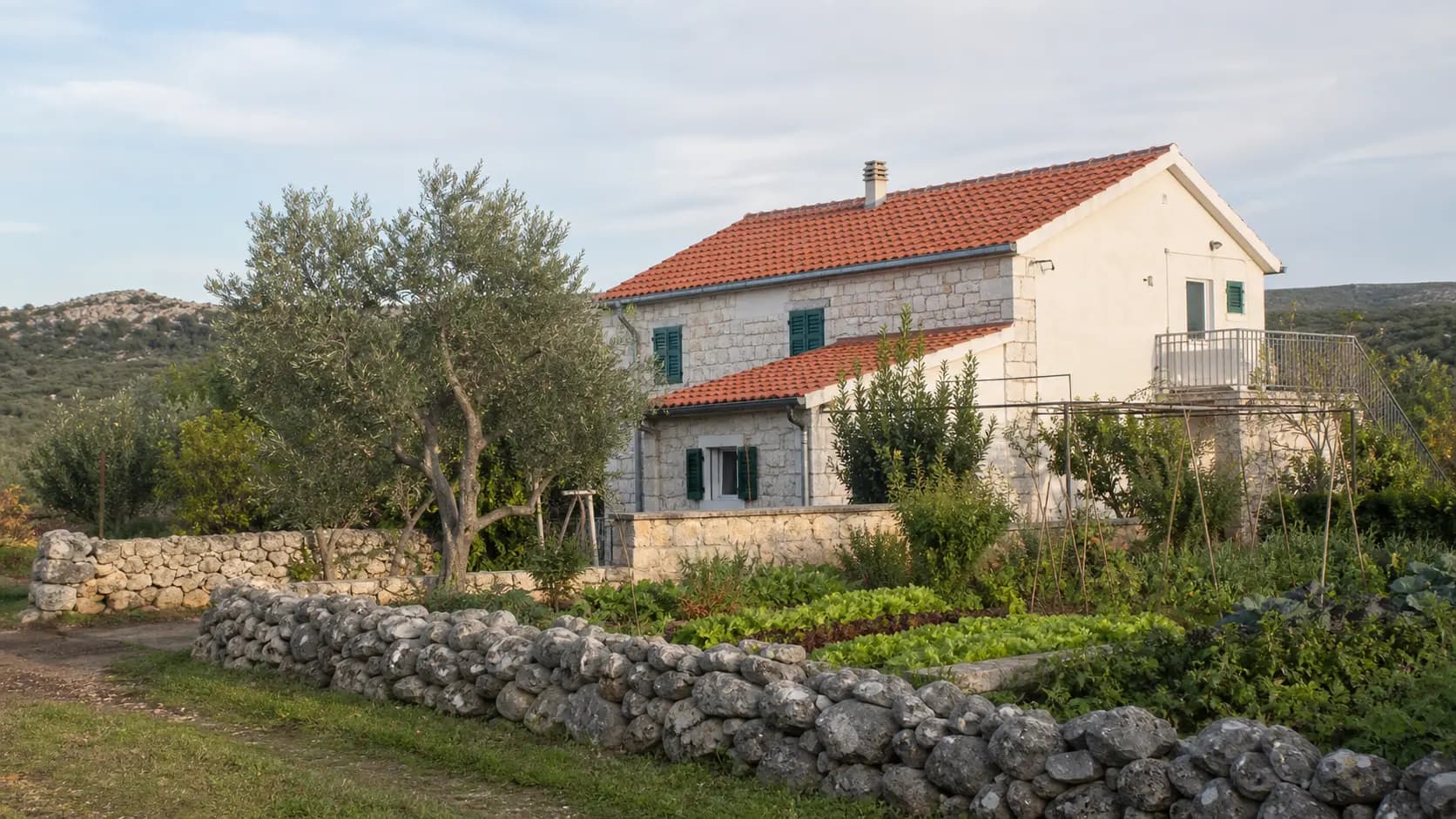 Illustrative family-home exterior with olive trees, a vegetable garden and a dry-stone wall in Dobra Voda’s rural setting.