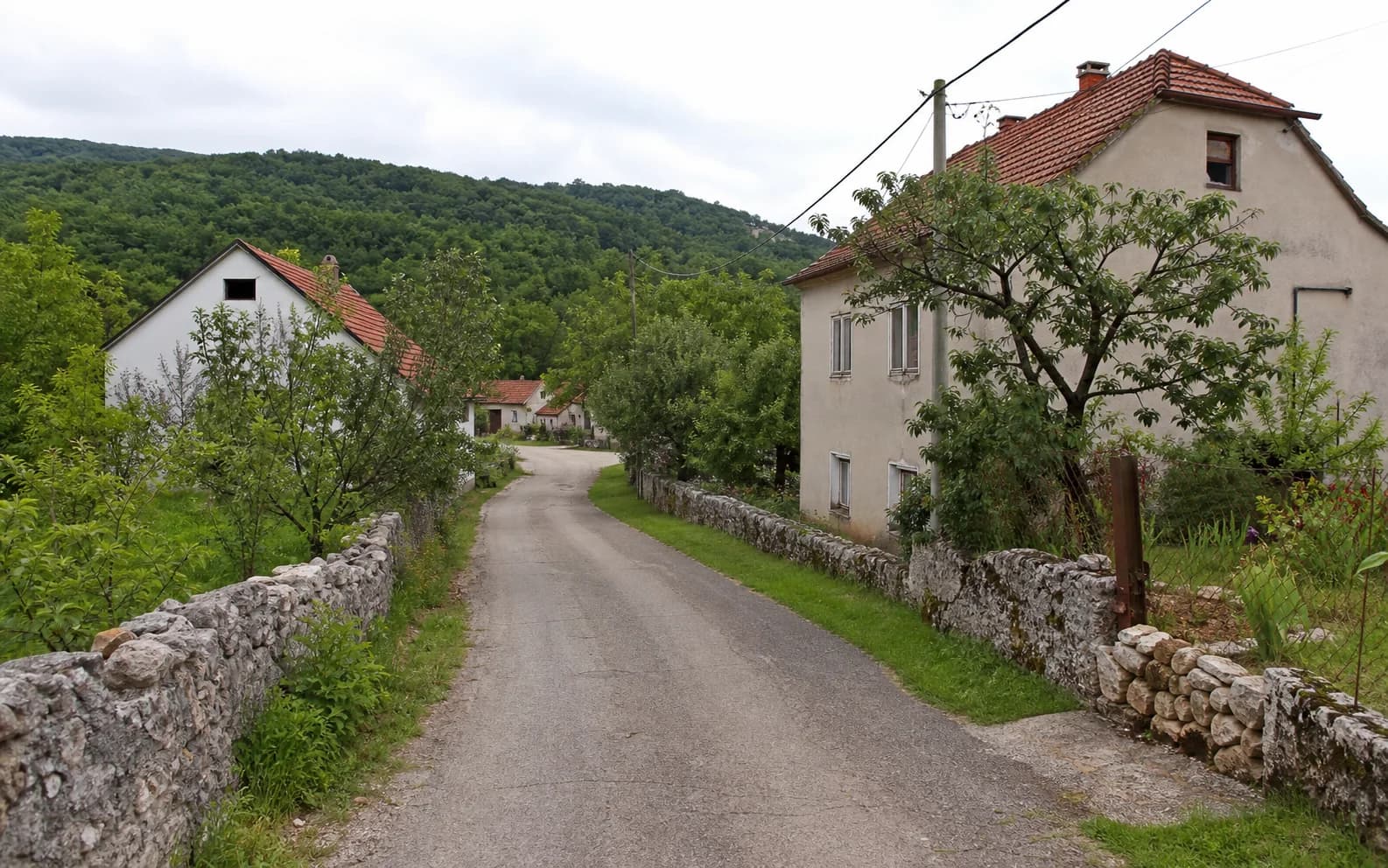 Illustratives Foto für Vučipolje, Gračac: ruhige Siedlungsstraße in hügeliger Umgebung.