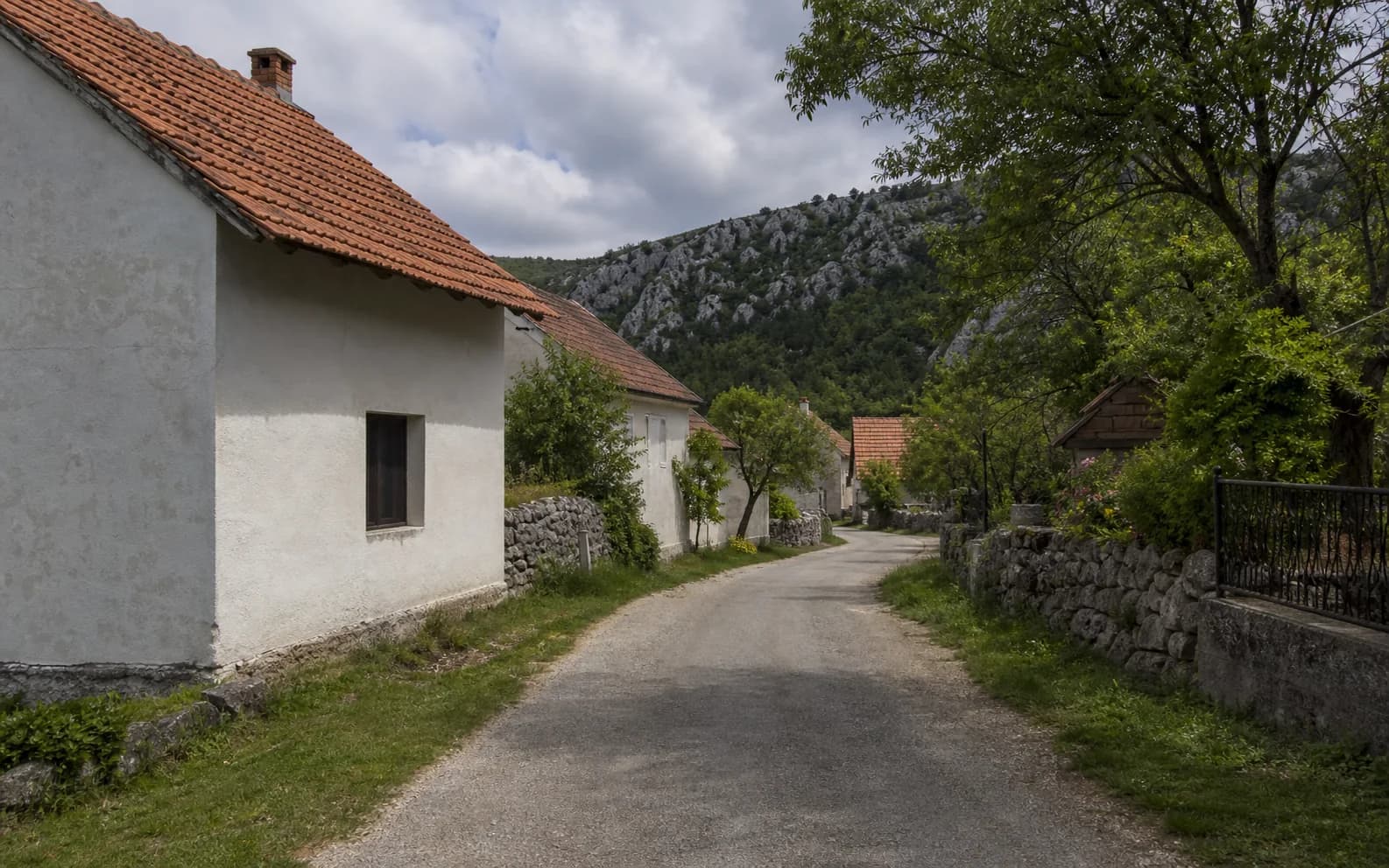 Illustratives Foto für Zrmanja Vrelo, Gračac: ruhige Siedlungsstraße in hügeliger Umgebung.