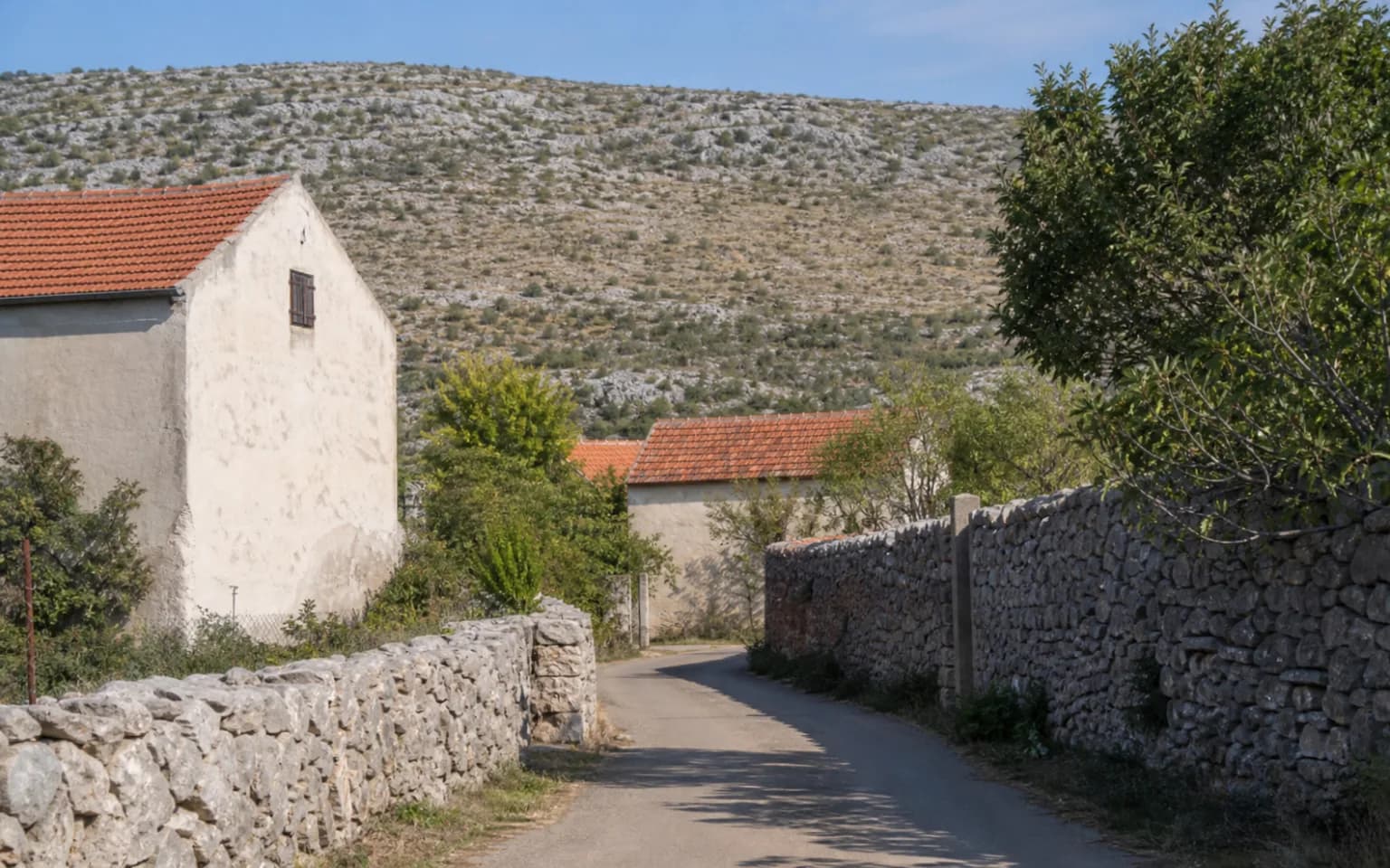 AI-generated illustrative village lane with stone walls, simple homes and a karst slope in the Komazeci setting.