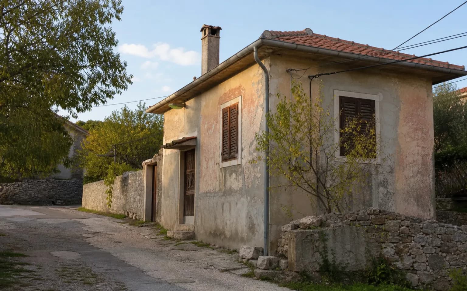 AI-generated illustrative exterior of a modest Dalmatian home with a weathered facade, shutters and a stone wall in the Komazeci setting.
