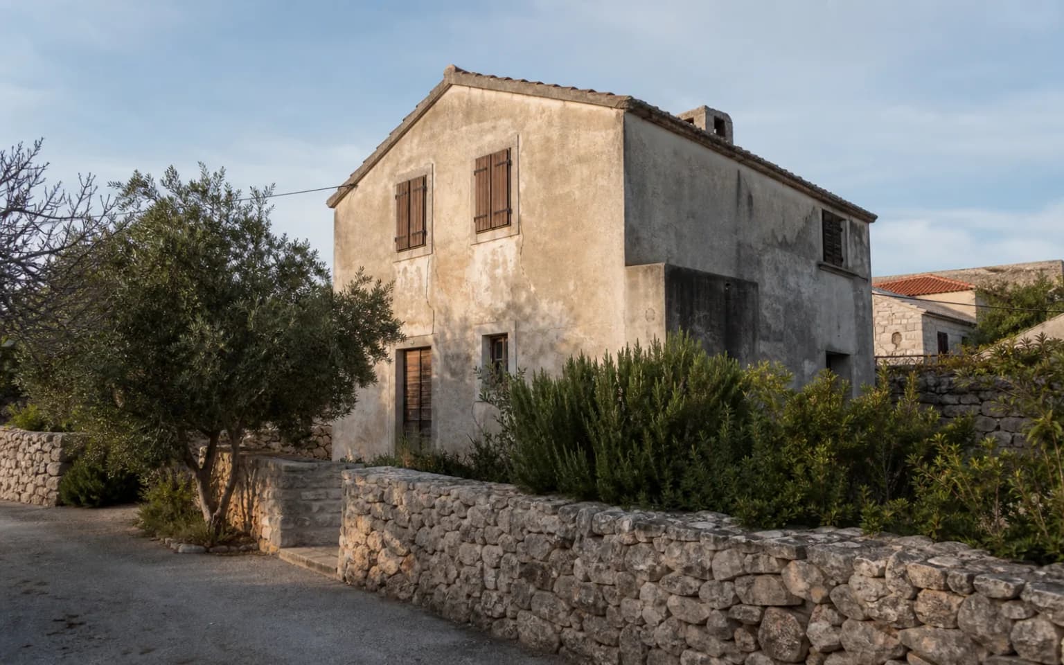 AI-generated illustrative exterior of a modest island home with a stone wall, wooden shutters and an olive tree in the Bošana setting.