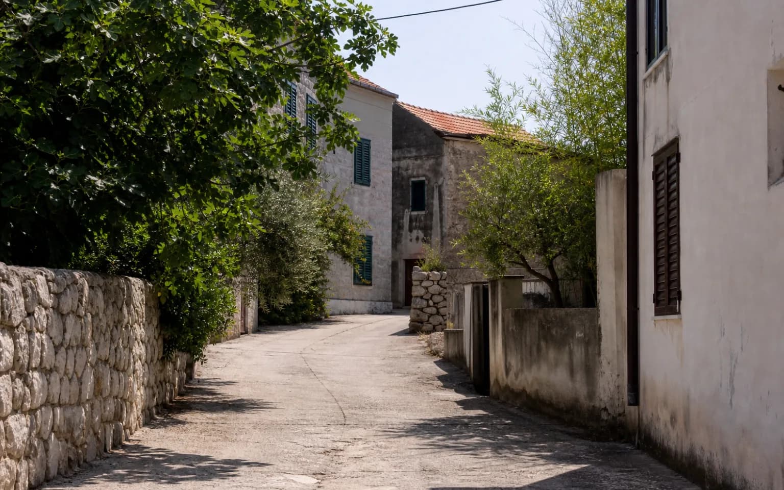 KI-generierte illustrative Insel-Dorfstraße mit Steinmauer, einfachen Fassaden und grünen Fensterläden im Ambiente von Miškovići.