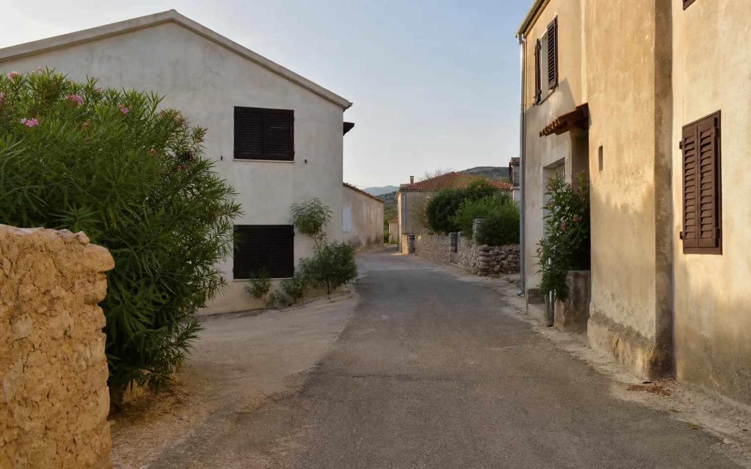 AI-generated illustrative quiet island lane with pale facades, a stone wall and wooden shutters in the Šimuni, Pag setting.