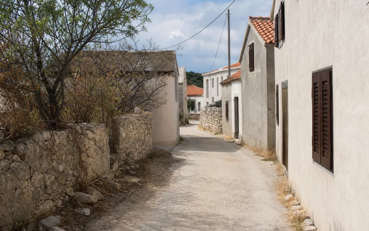KI-generierte illustrative ruhige Inselgasse mit Steinmauer, hellen Fassaden und alten Fensterläden im Ambiente von Stara Vas auf Pag.