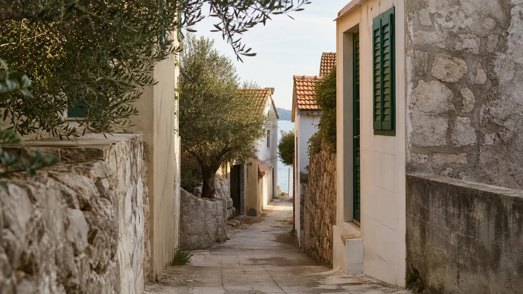 Ilustrativna mirna kamena ulica s mediteranskim kućama i pogledom prema moru u Banju.